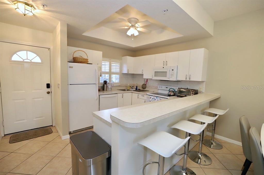 A kitchen features white cabinets, a breakfast bar with stools, and a white refrigerator — 8370 WINGATE DRIVE UNIT 714, SARASOTA, FL