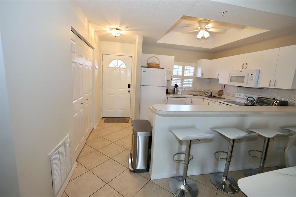 A kitchen with white cabinets, a breakfast bar with three stools, and a tiled entryway — 8370 WINGATE DRIVE UNIT 714, SARASOTA, FL