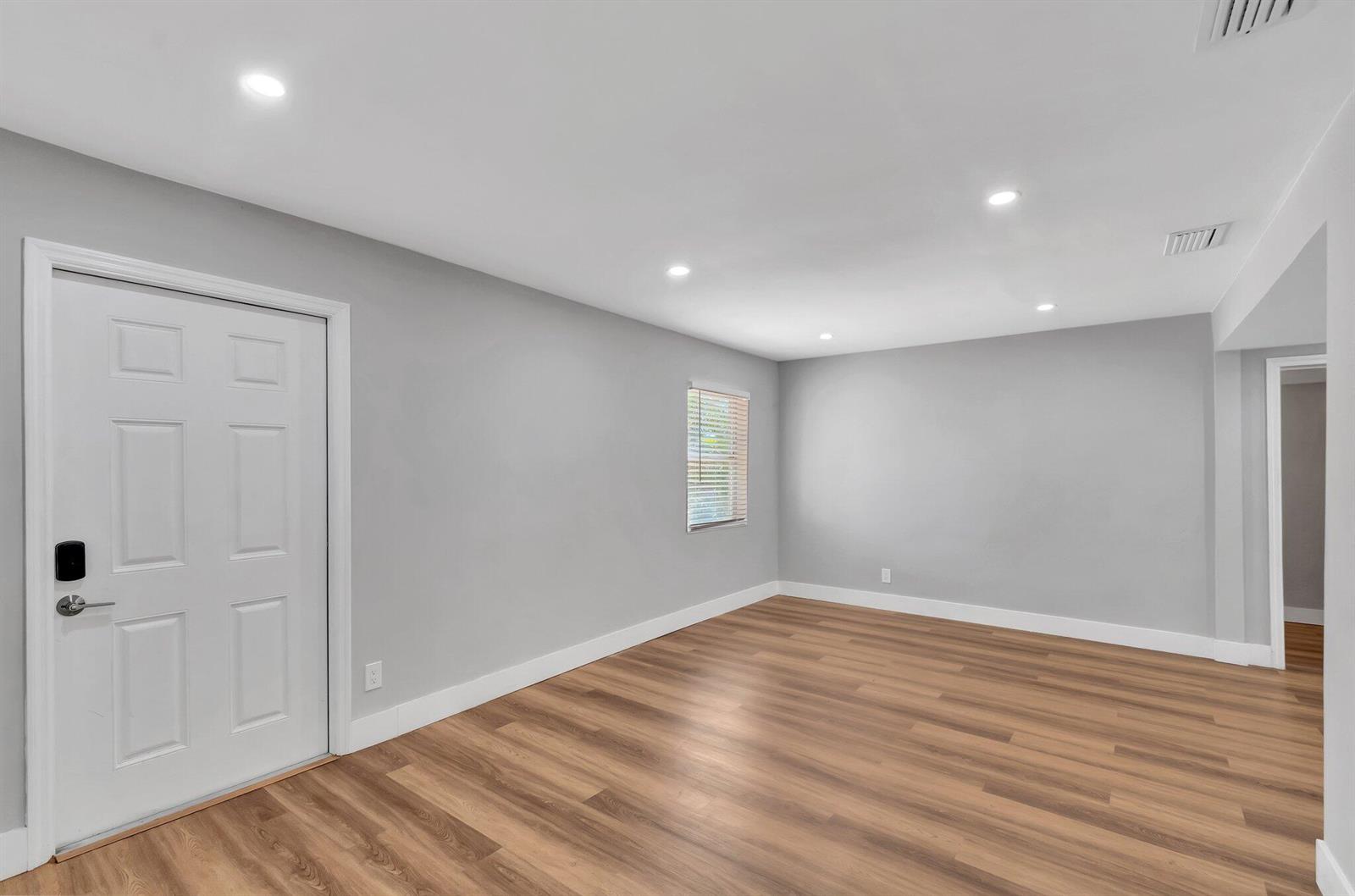 An empty room features light gray walls, wood-look flooring, recessed lighting, and a white door — 125 E Hart Street, Lantana FL 33462, LANTANA, FL