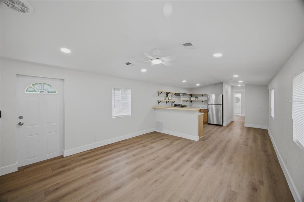 An open-concept living area features light wood-look flooring, white walls, and a kitchen peninsula — 11602 LEWIS AVENUE, THONOTOSASSA, FL