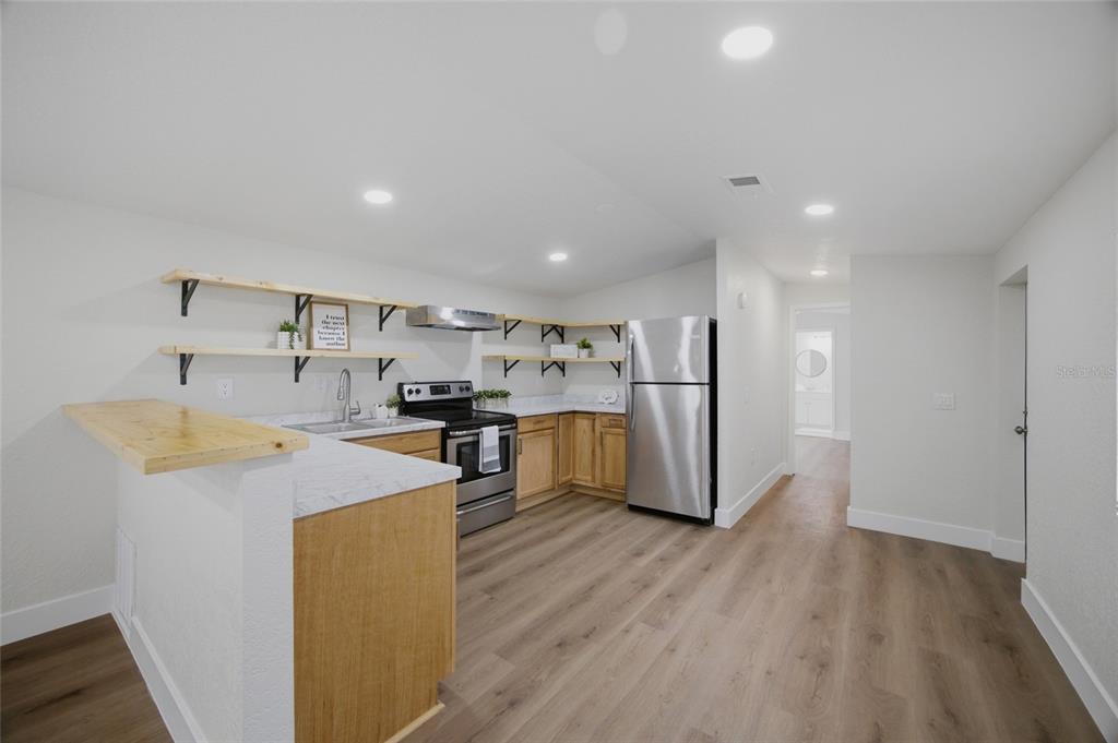 A kitchen features light wood cabinets, open shelving, stainless steel appliances, and a breakfast bar — 11602 LEWIS AVENUE, THONOTOSASSA, FL