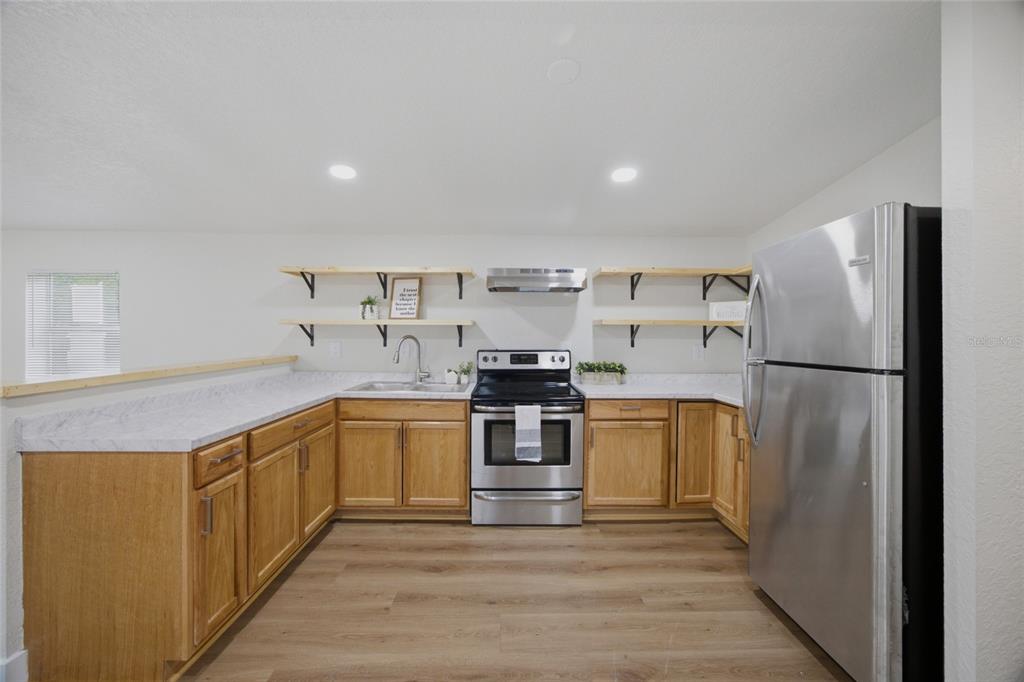A kitchen features light wood cabinets, white marble-look countertops, open shelving, and stainless steel appliances — 11602 LEWIS AVENUE, THONOTOSASSA, FL