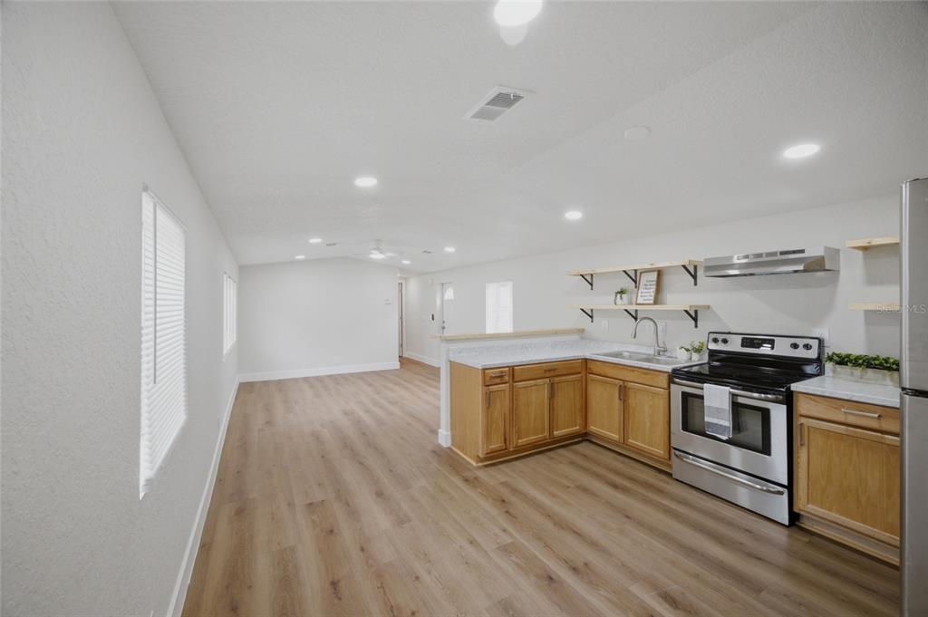 An open-concept kitchen and living area features light wood flooring and natural wood cabinets — 11602 LEWIS AVENUE, THONOTOSASSA, FL