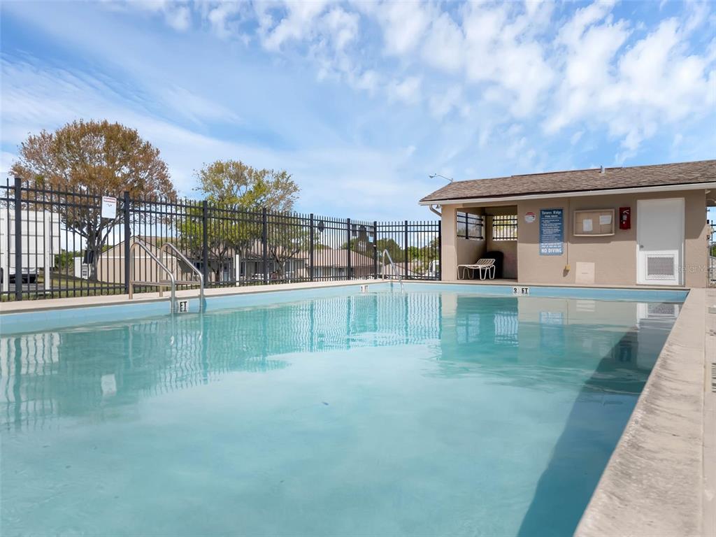 A rectangular outdoor swimming pool sits in front of a small building with a fence — 30213 TAVARES RIDGE BOULEVARD UNIT 30213, TAVARES, FL