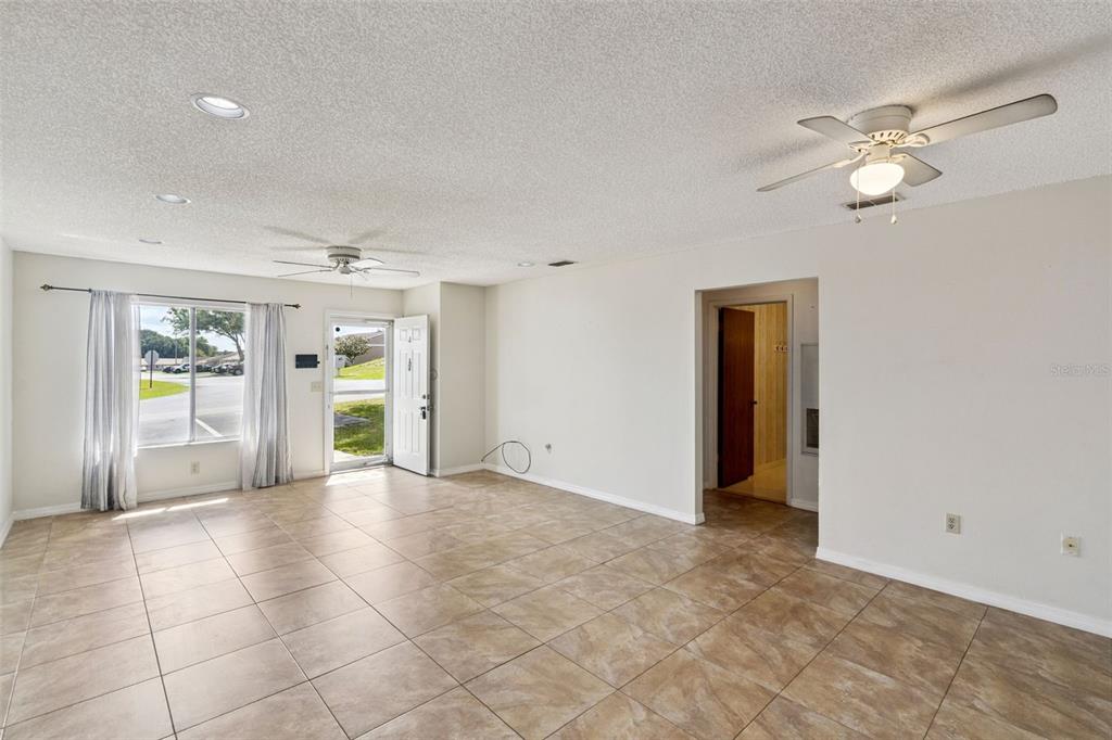 A living room with beige tile flooring, white walls, two ceiling fans, and a doorway — 30213 TAVARES RIDGE BOULEVARD UNIT 30213, TAVARES, FL