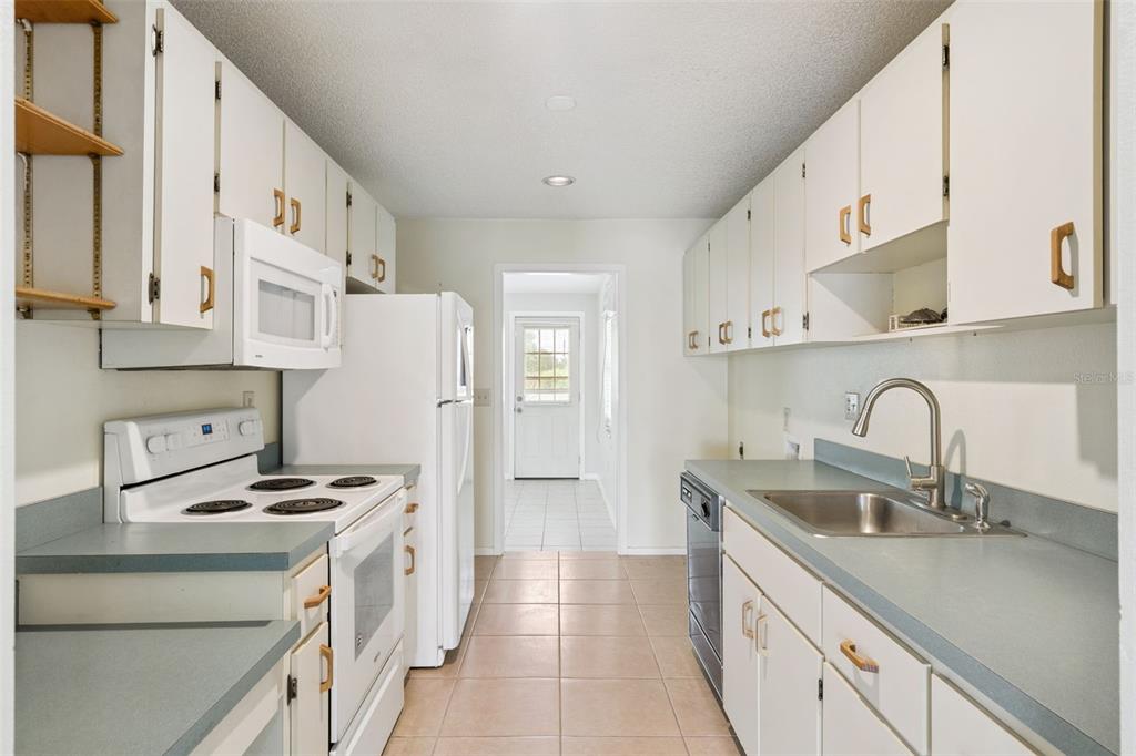 A galley-style kitchen features white cabinets, blue countertops, a white stove, and tile flooring — 30213 TAVARES RIDGE BOULEVARD UNIT 30213, TAVARES, FL