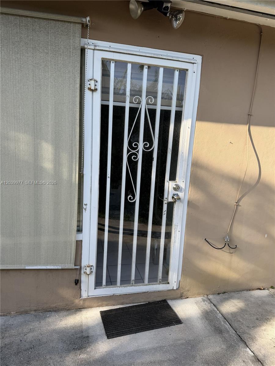 A white metal security screen door is installed on the exterior of a tan building — MIAMI, FL