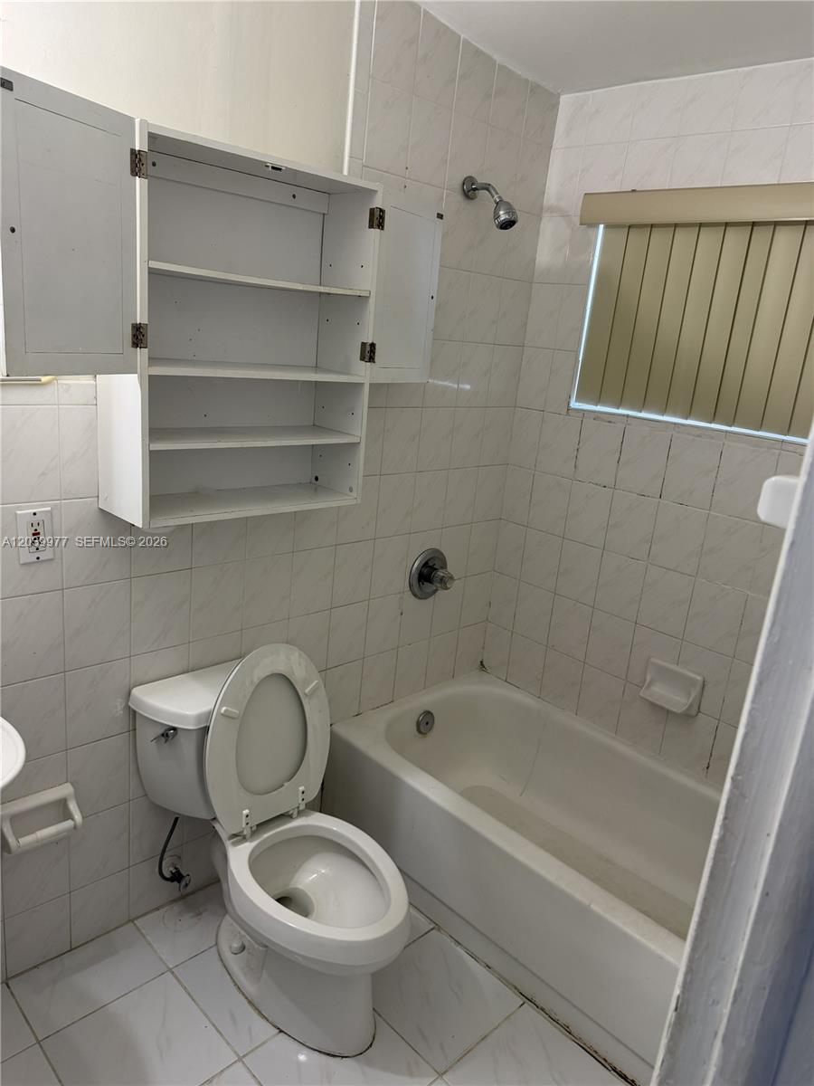 A bathroom features a white toilet, a bathtub with a showerhead, and wall-mounted shelving — MIAMI, FL