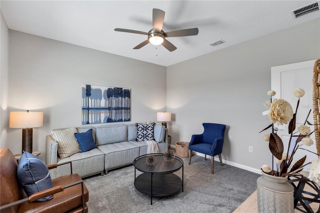 A living room features a gray sectional sofa, a blue armchair, and a ceiling fan — 6032 MEDITATION DRIVE, CLERMONT, FL