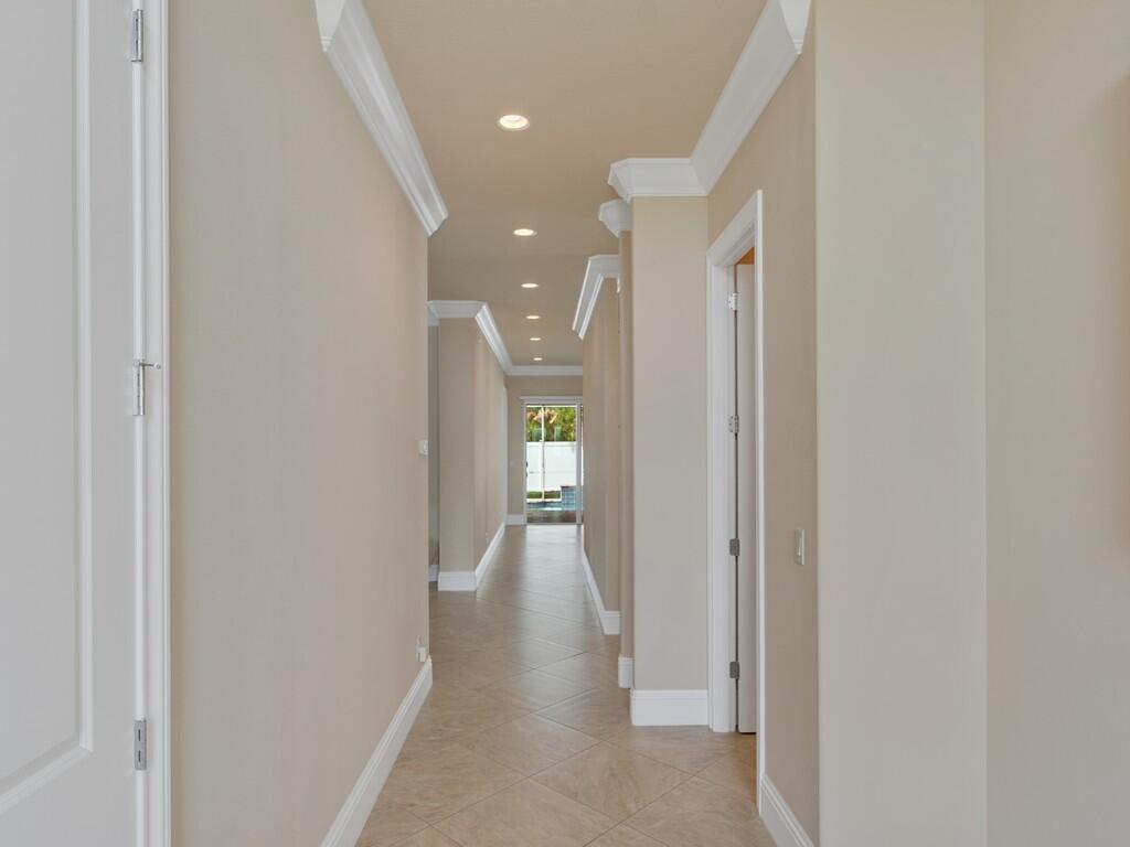 A long hallway with beige walls, crown molding, and tiled flooring leads to an exterior door — 445 Wingate Terrace SW, Vero Beach FL 32968, VERO BEACH, FL