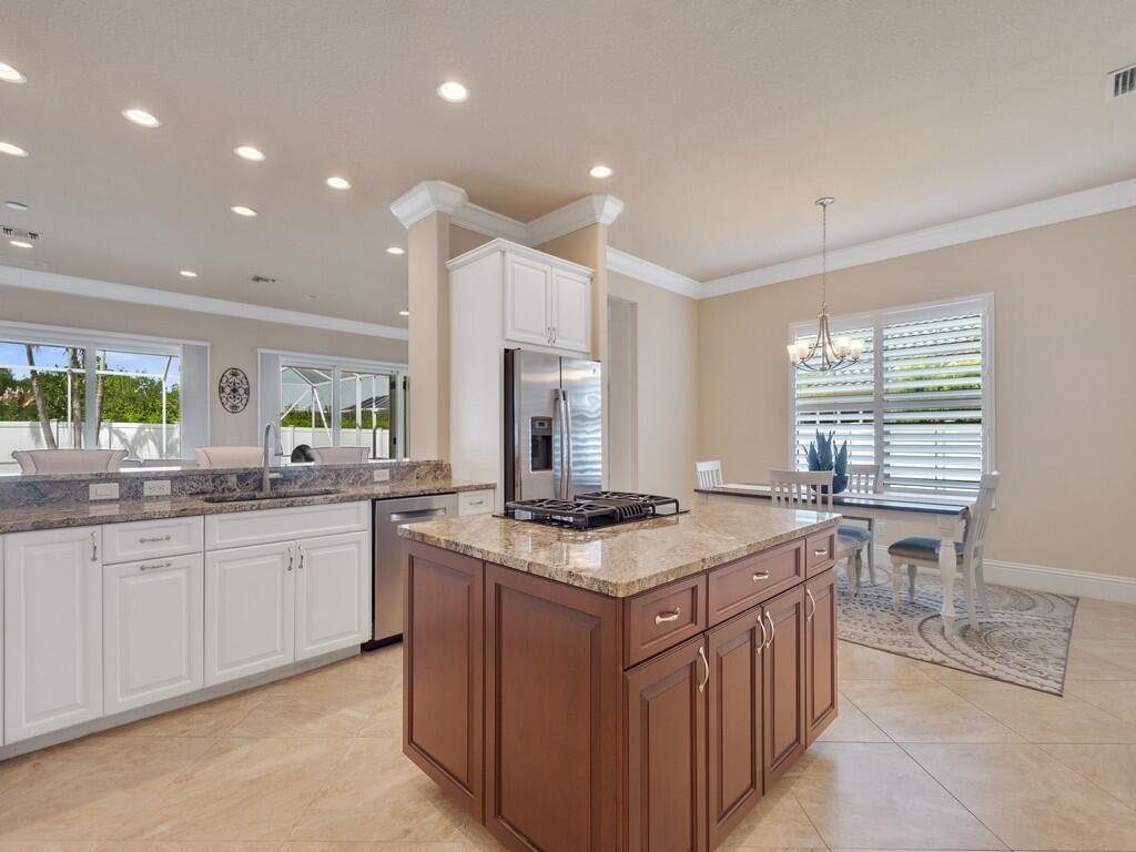 A kitchen features a dark wood island, white perimeter cabinets, granite countertops, and a dining area — 445 Wingate Terrace SW, Vero Beach FL 32968, VERO BEACH, FL