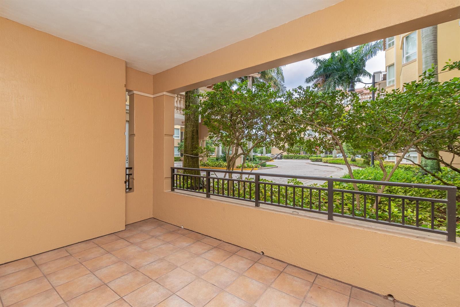 A covered balcony with tan walls, tiled flooring, and a dark metal railing overlooking trees — 16101 Emerald Estates Drive # 146, Weston FL 33331, WESTON, FL