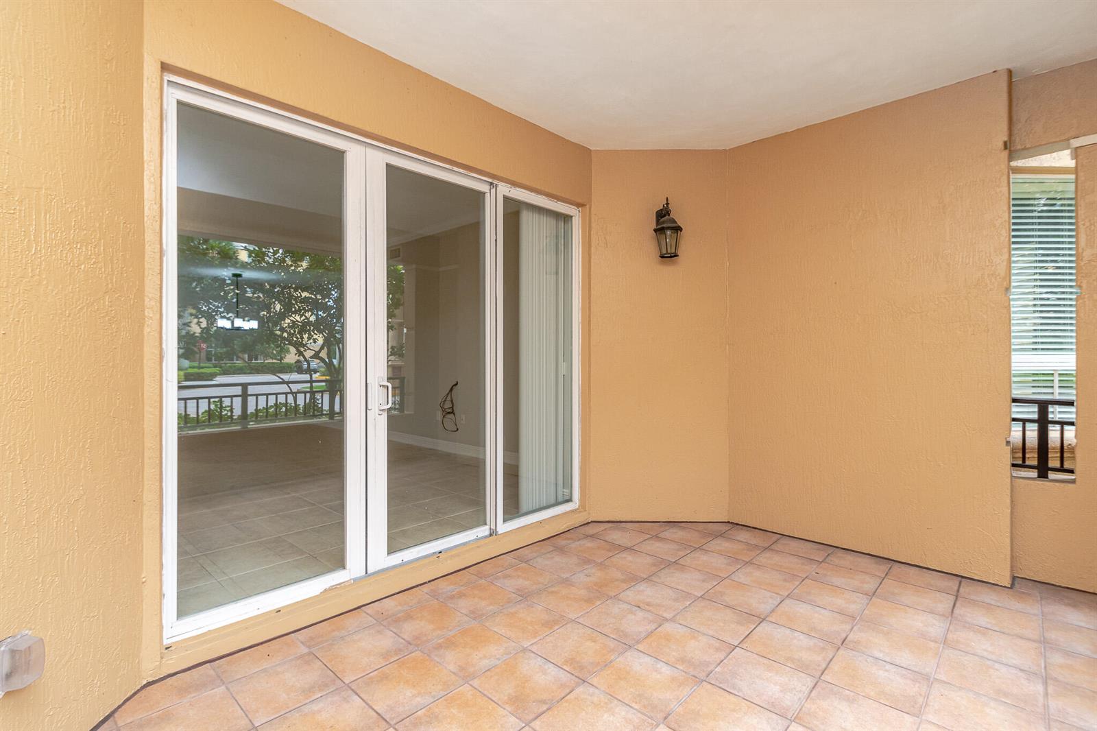 A covered patio features tan stucco walls, tiled flooring, a wall-mounted lantern, and sliding glass doors — 16101 Emerald Estates Drive # 146, Weston FL 33331, WESTON, FL