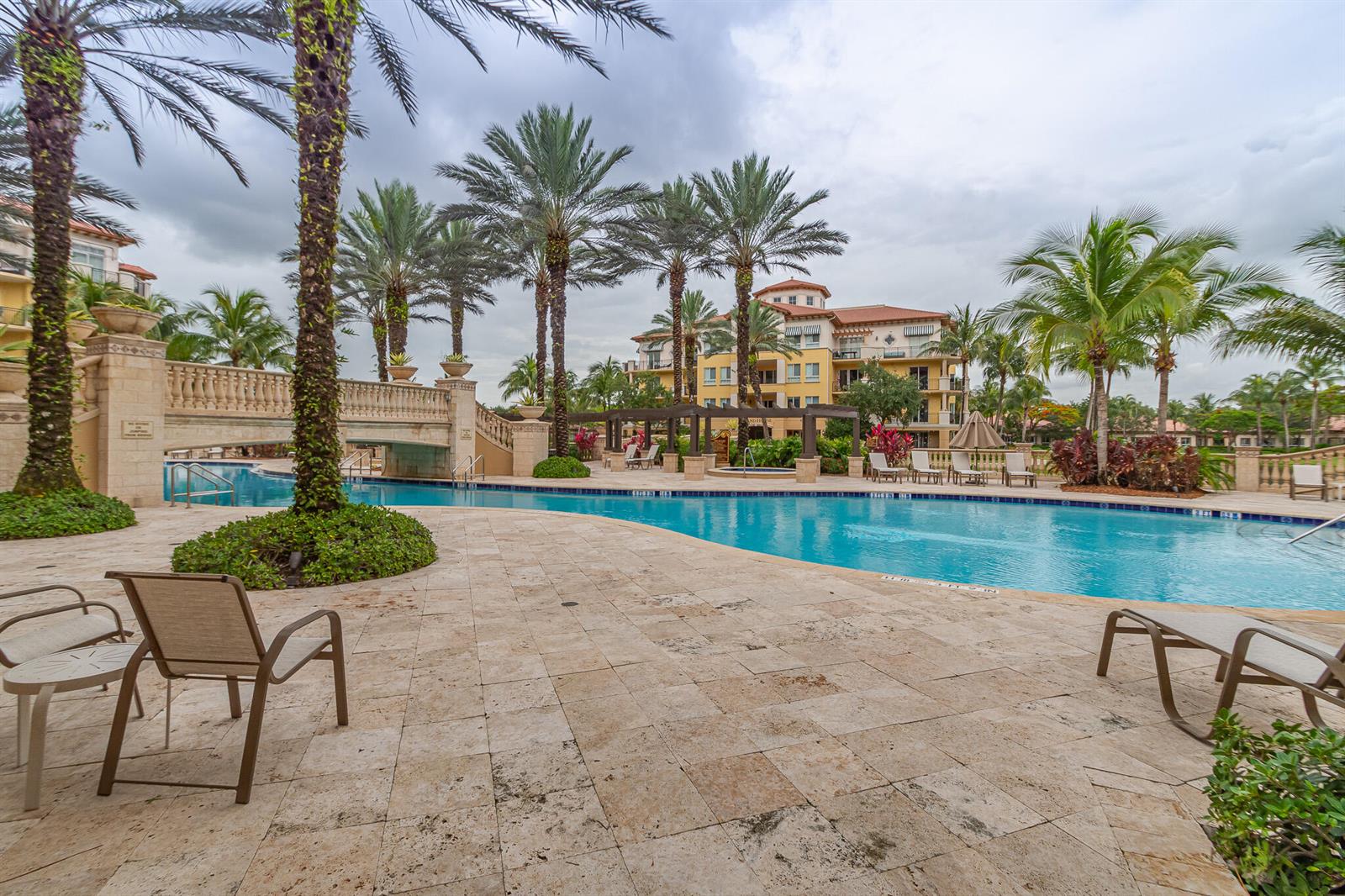 A swimming pool with a stone bridge and palm trees in front of a building — 16101 Emerald Estates Drive # 146, Weston FL 33331, WESTON, FL