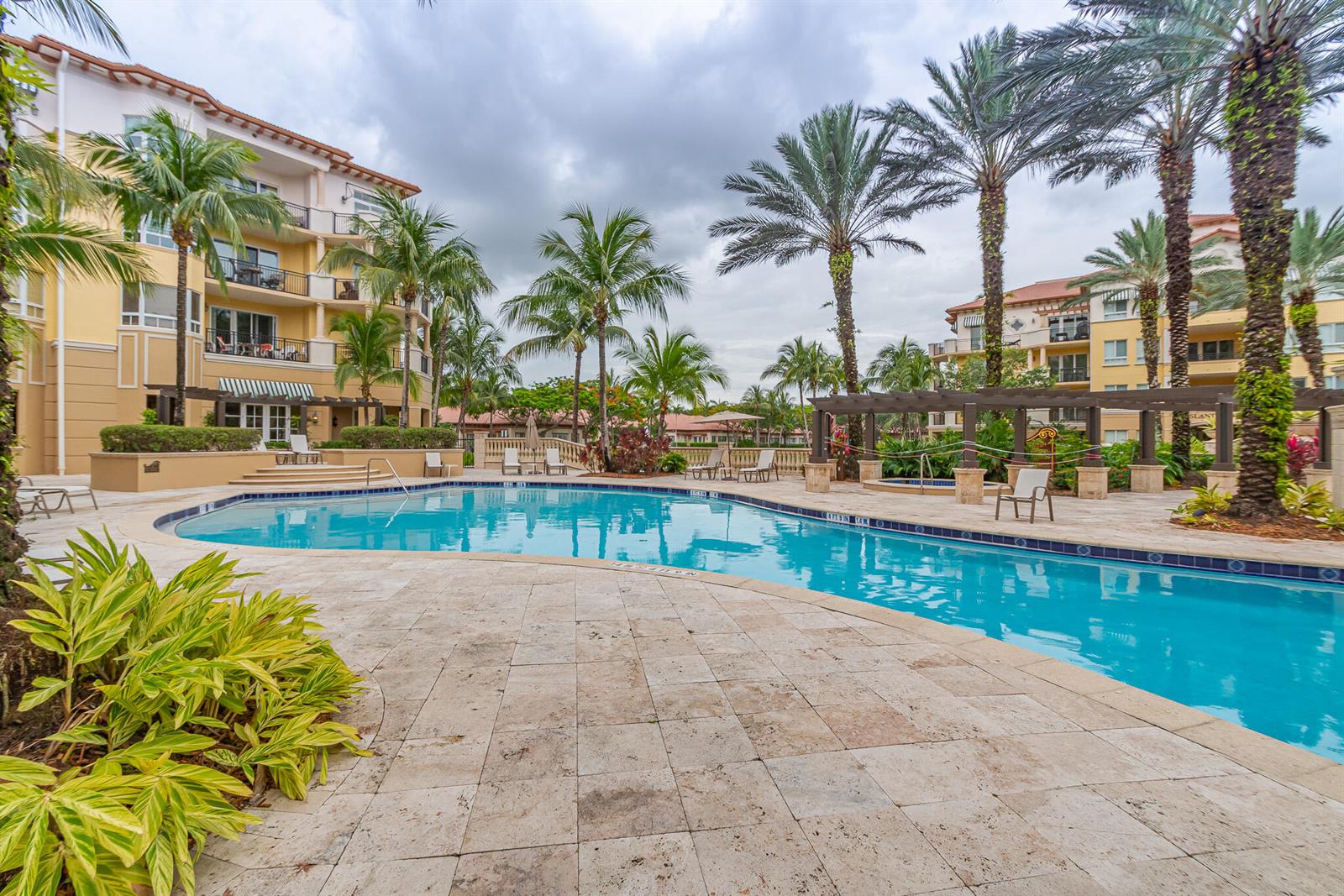 A swimming pool surrounded by a stone patio, palm trees, and multi-story residential buildings — 16101 Emerald Estates Drive # 146, Weston FL 33331, WESTON, FL