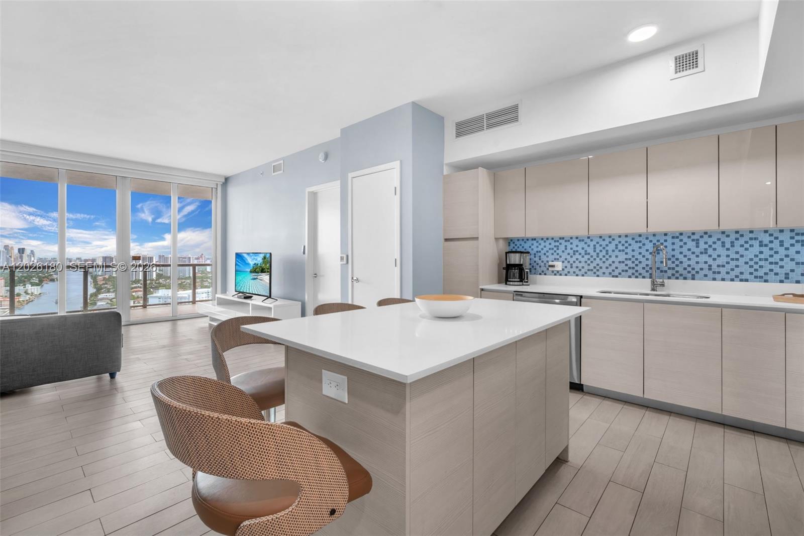 A modern kitchen with a white island and light wood cabinetry opens to a living area — 2602 E E HALLADALE # T3105, Hallandale Beach FL 33009, HALLANDALE BEACH, FL