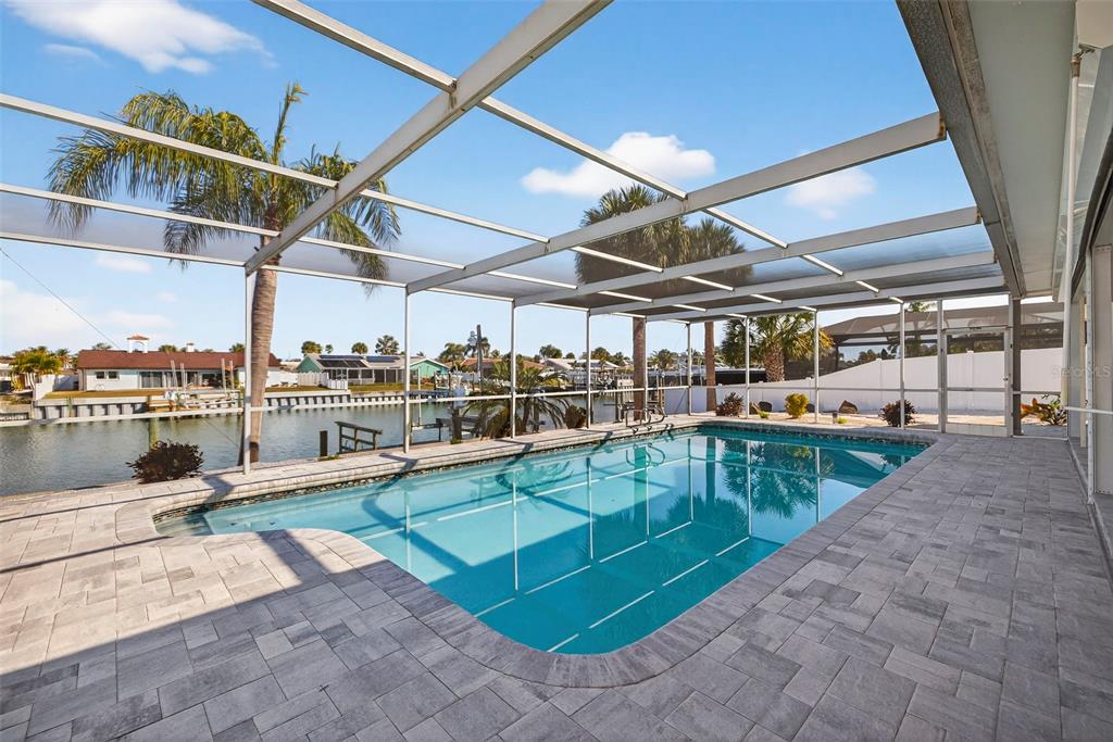 A screened-in swimming pool patio overlooks a canal with houses in the background — 4426 43RD STREET S, ST PETERSBURG, FL