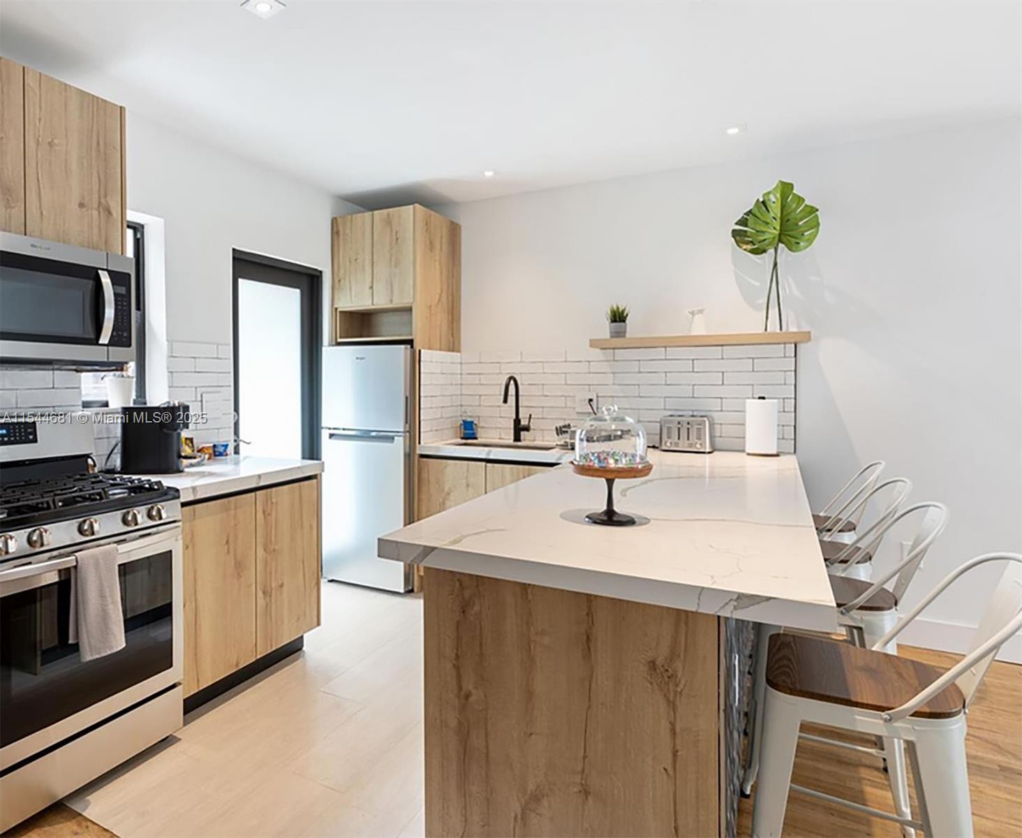 A modern kitchen features light wood cabinets, white countertops, a central island, and white subway tiles — 740 SW 9th St # 1, Miami FL 33130, MIAMI, FL