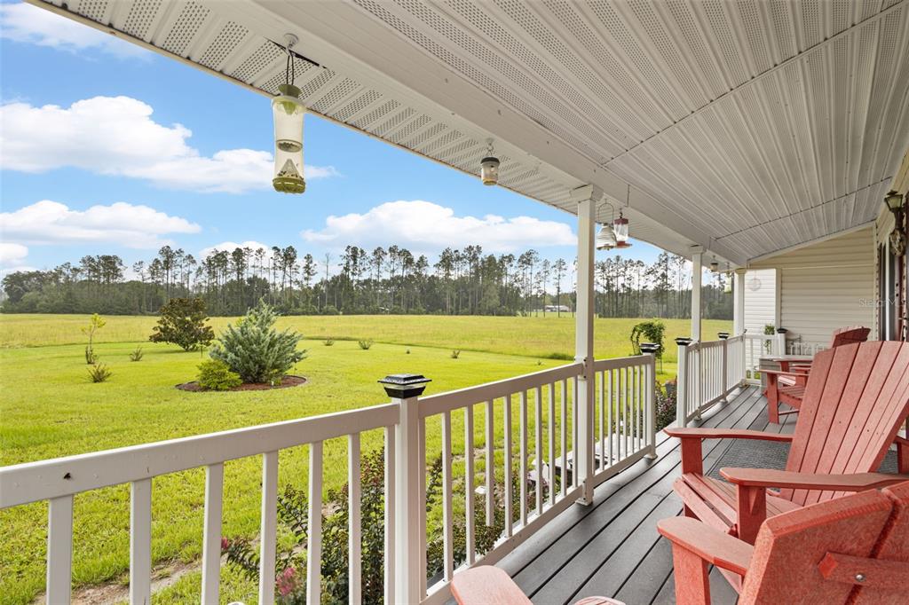 A covered porch with red Adirondack chairs overlooks a large grassy field and distant trees — 4700 NW 26TH STREET, BELL, FL