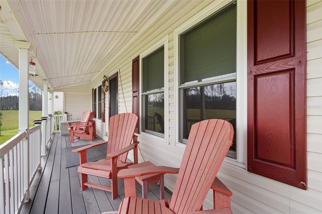 A covered porch features gray decking, red Adirondack chairs, and light-colored vinyl siding — 4700 NW 26TH STREET, BELL, FL