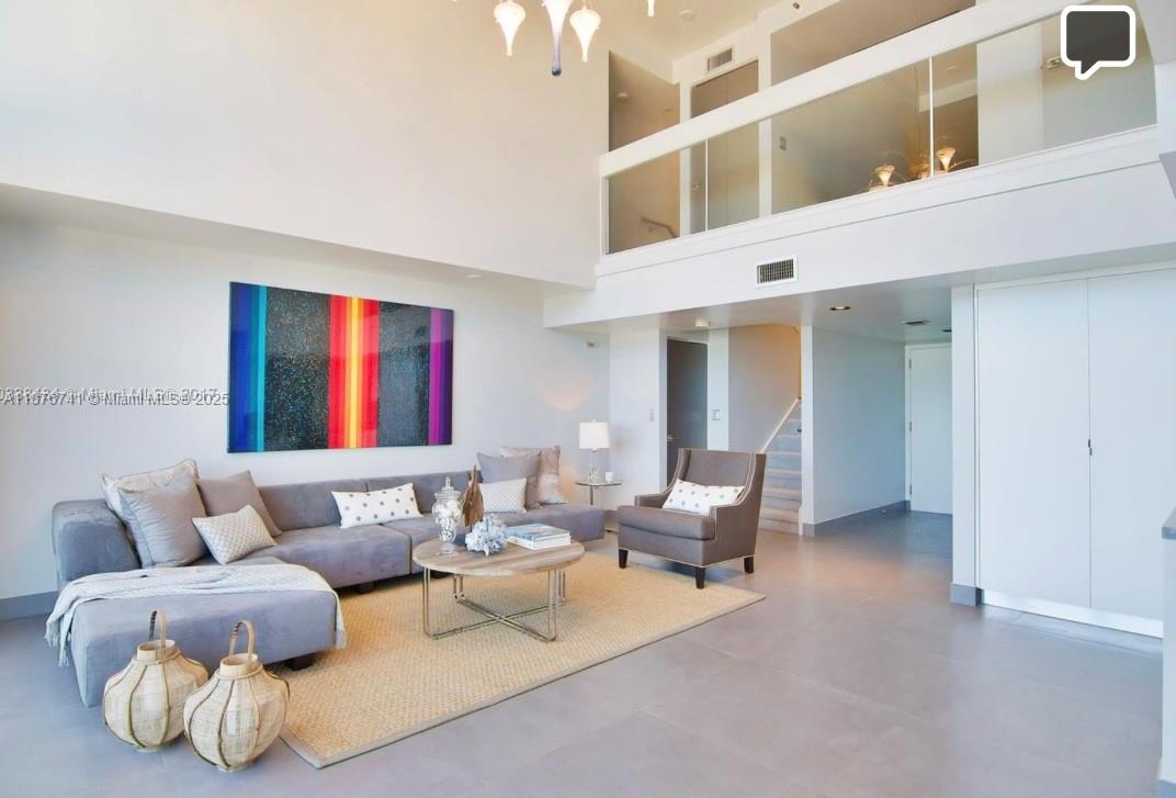 A living room with high ceilings, a grey sectional sofa, and a glass-railed loft above — 151 SE 15th Rd # 2703, Miami FL 33129, MIAMI, FL