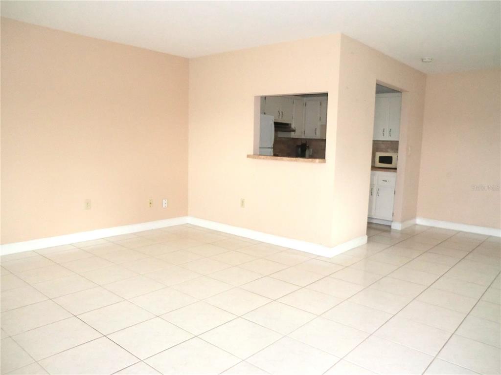 An empty room with light-colored tile flooring and a pass-through window to the kitchen — 201 KINGS BOULEVARD UNIT 15, SUN CITY CENTER, FL