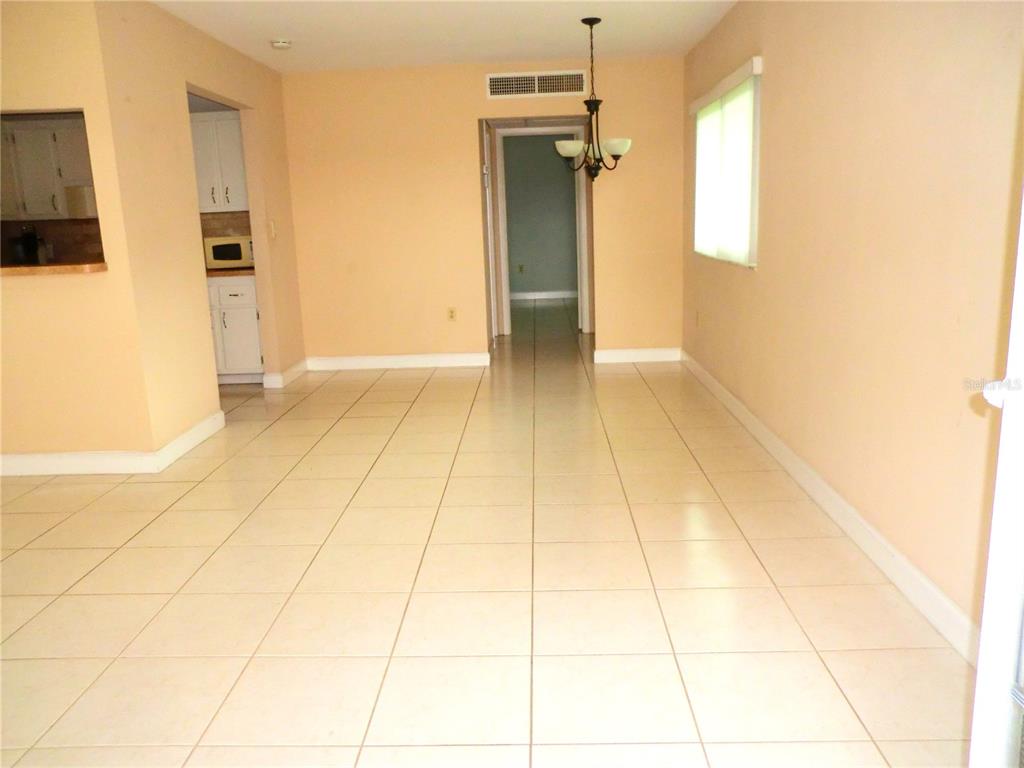 A dining area with light-colored tile flooring, peach walls, and a hanging chandelier — 201 KINGS BOULEVARD UNIT 15, SUN CITY CENTER, FL