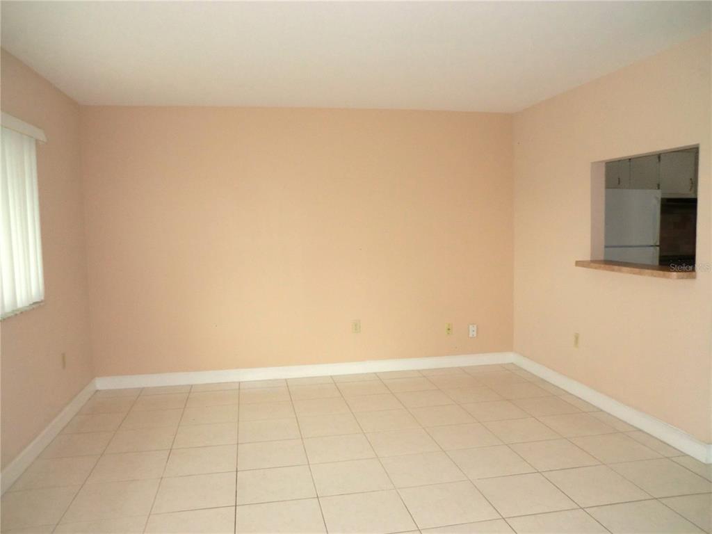 An empty room features light-colored tile flooring, beige walls, and a pass-through window — 201 KINGS BOULEVARD UNIT 15, SUN CITY CENTER, FL