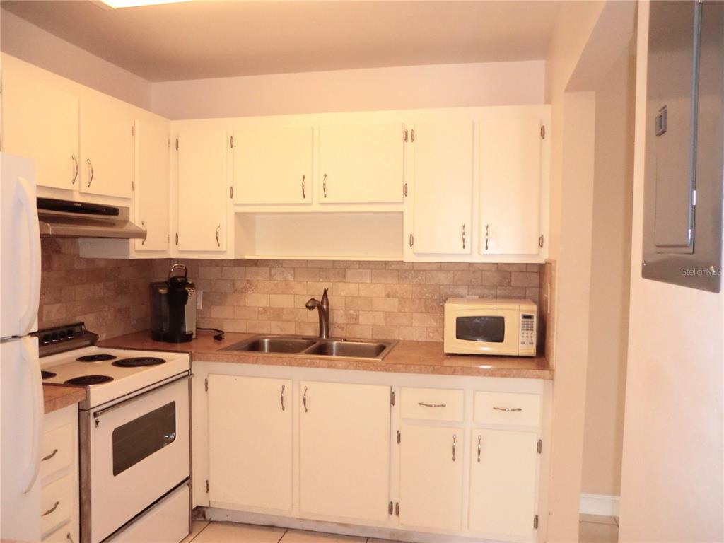 A kitchen with white cabinets, a double sink, a tan countertop, and a tiled backsplash — 201 KINGS BOULEVARD UNIT 15, SUN CITY CENTER, FL