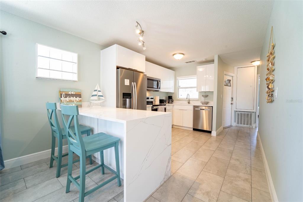 A kitchen with white cabinets, stainless steel appliances, and a marble-topped island with two chairs — 4825 FLORAMAR TERRACE, NEW PORT RICHEY, FL