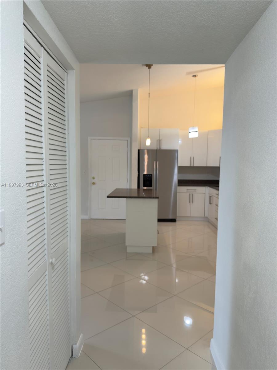 A kitchen with white cabinets, stainless steel appliances, and a small island with tile flooring — 907 NE 199th St # 204, Miami FL 33179, MIAMI, FL