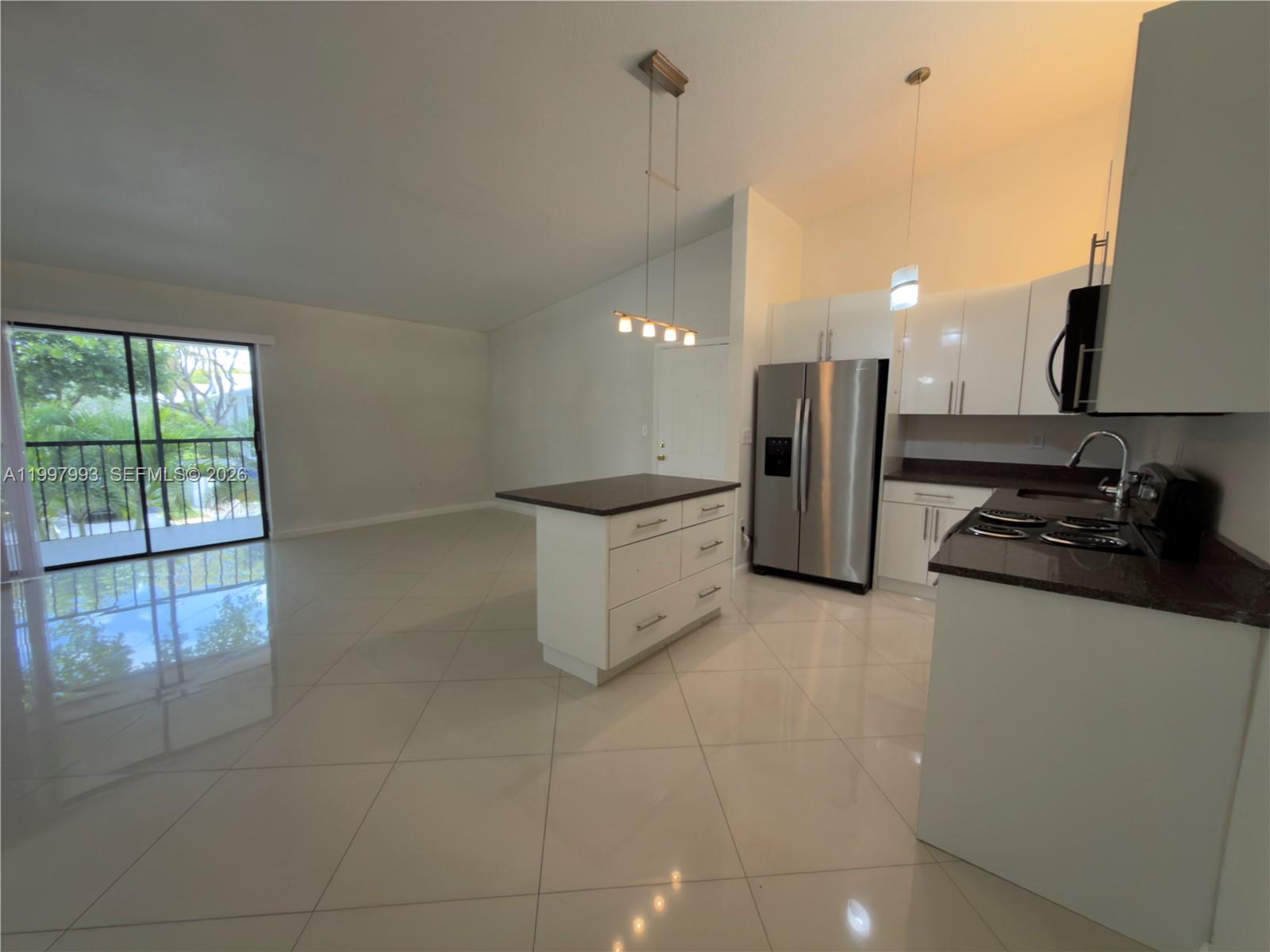 A kitchen with white cabinets and a center island opens to a living area — 907 NE 199th St # 204, Miami FL 33179, MIAMI, FL