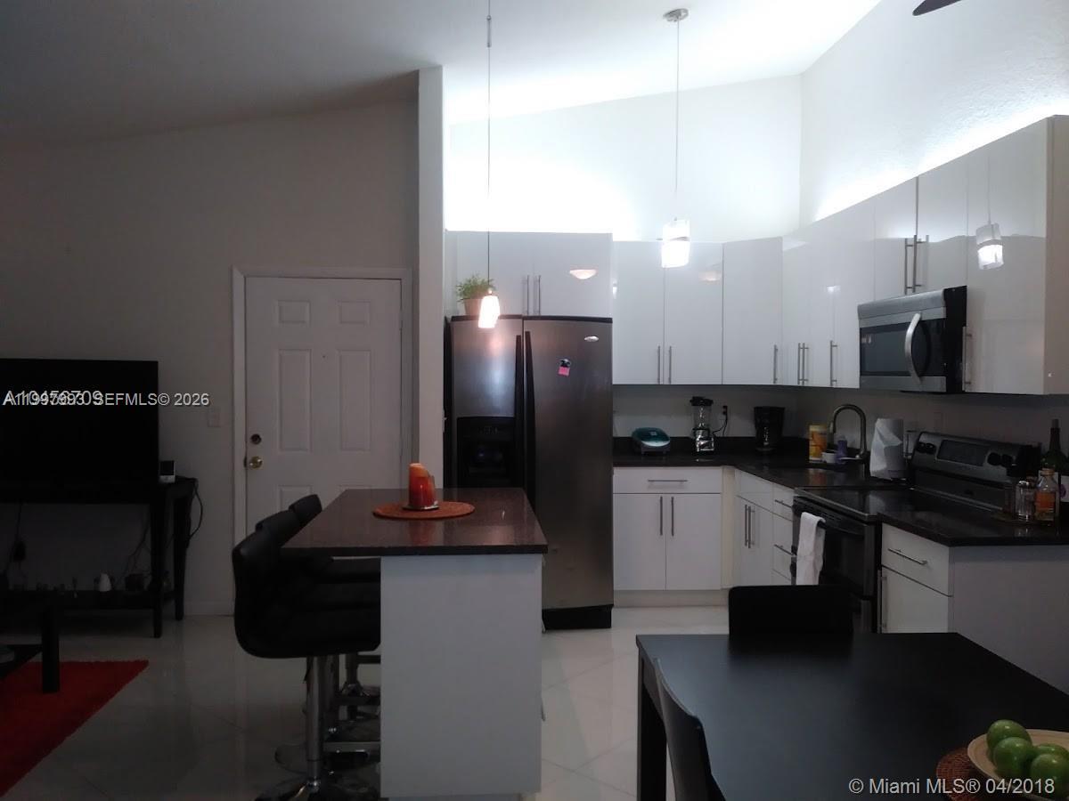 A modern kitchen features white cabinets, stainless steel appliances, and a small breakfast bar island — 907 NE 199th St # 204, Miami FL 33179, MIAMI, FL