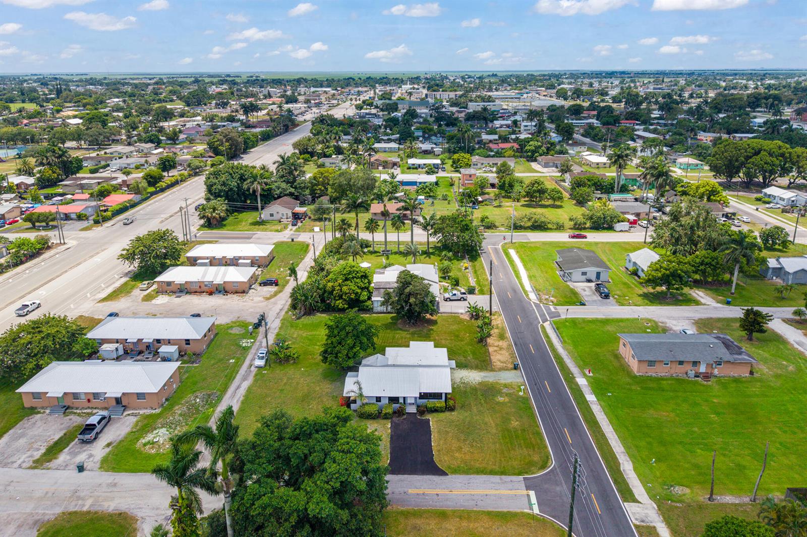 An aerial view shows a residential neighborhood with several houses, palm trees, and paved roads — 24 NW Avenue I, Belle Glade FL 33430, BELLE GLADE, FL