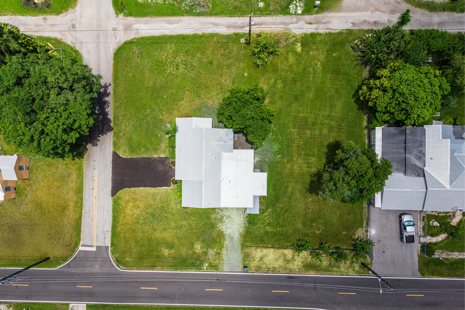 An aerial view shows a house with a metal roof, a driveway, and large lawns — 24 NW Avenue I, Belle Glade FL 33430, BELLE GLADE, FL