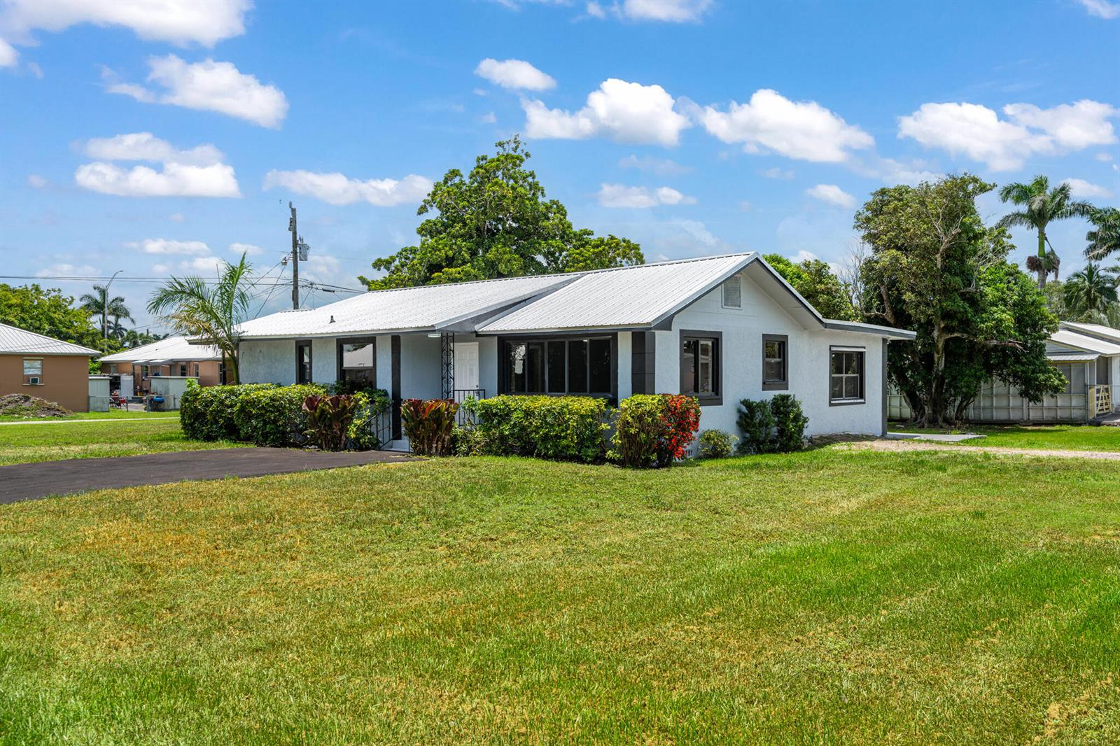 A single-story house with a white metal roof and a large front lawn — 24 NW Avenue I, Belle Glade FL 33430, BELLE GLADE, FL