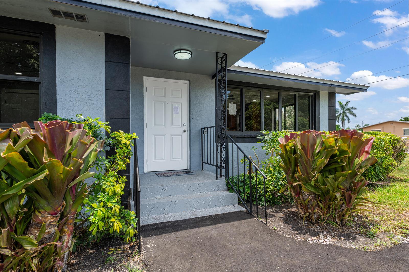 The exterior of a house features a white front door, concrete steps, and large bromeliads — 24 NW Avenue I, Belle Glade FL 33430, BELLE GLADE, FL
