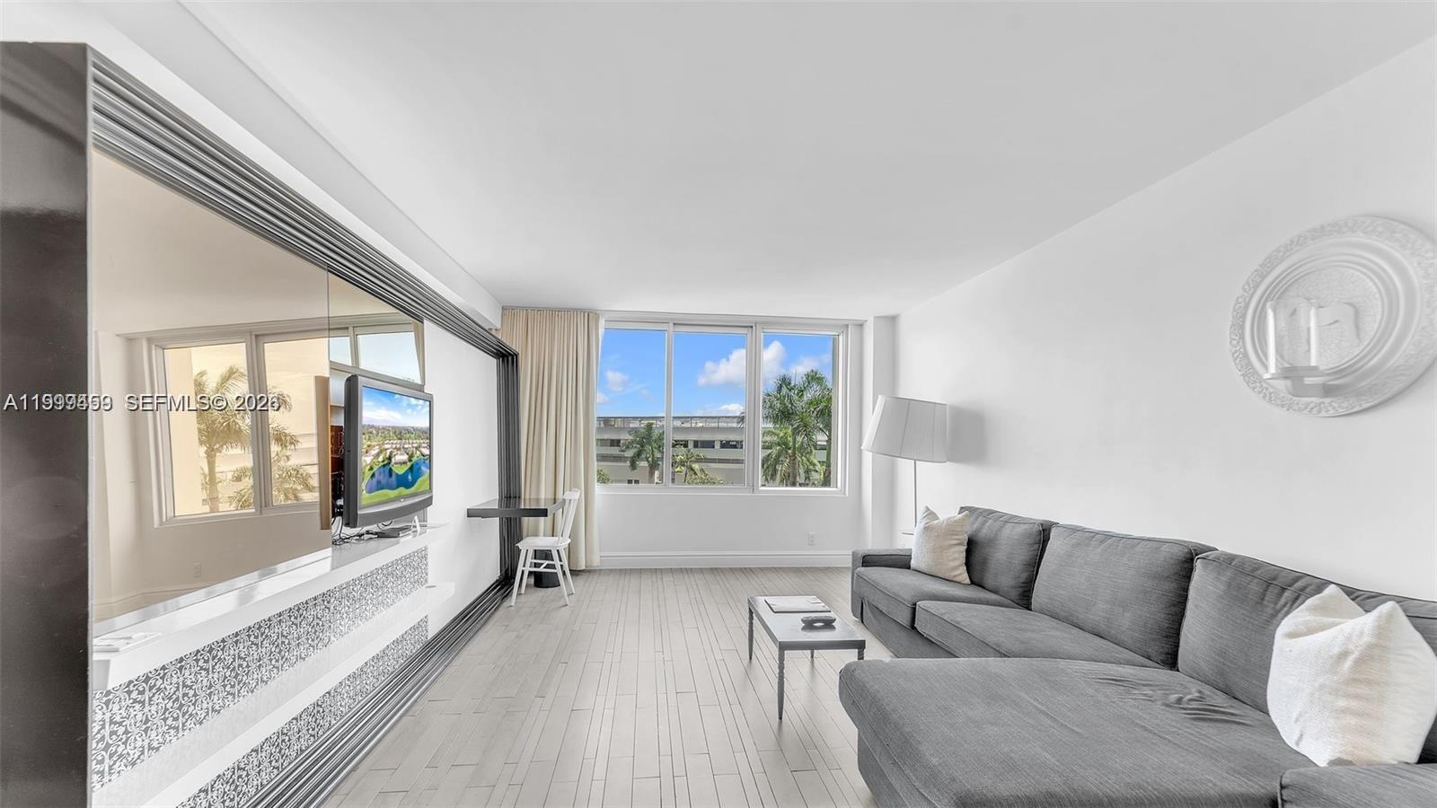 A living room features a grey sectional sofa, light wood flooring, and a large wall mirror — 1100 West Ave # 409, Miami Beach FL 33139, MIAMI BEACH, FL