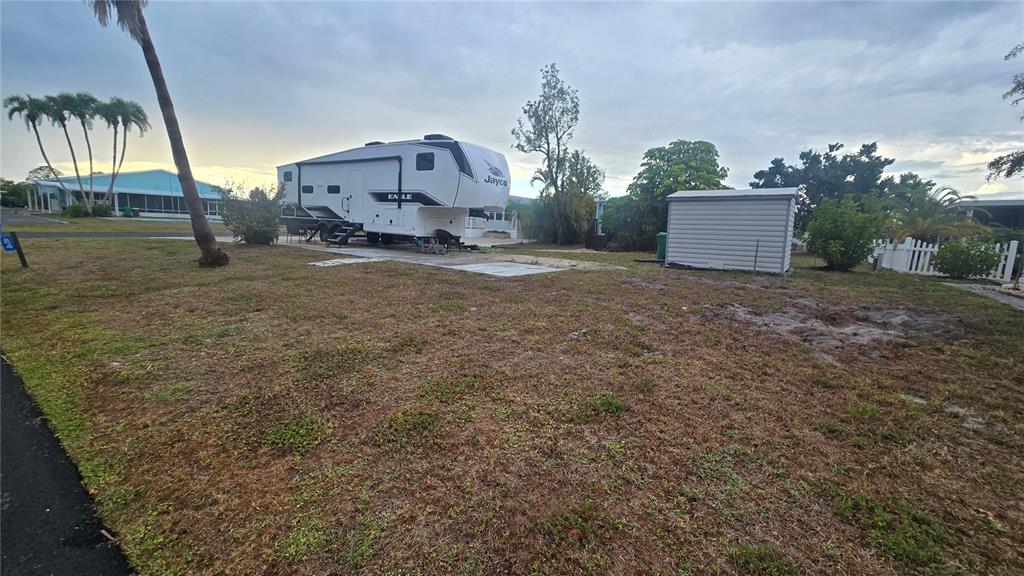 A white Jayco fifth-wheel trailer sits on a grassy lot next to a storage shed — 6767 SAN CASA DRIVE UNIT 84, ENGLEWOOD, FL