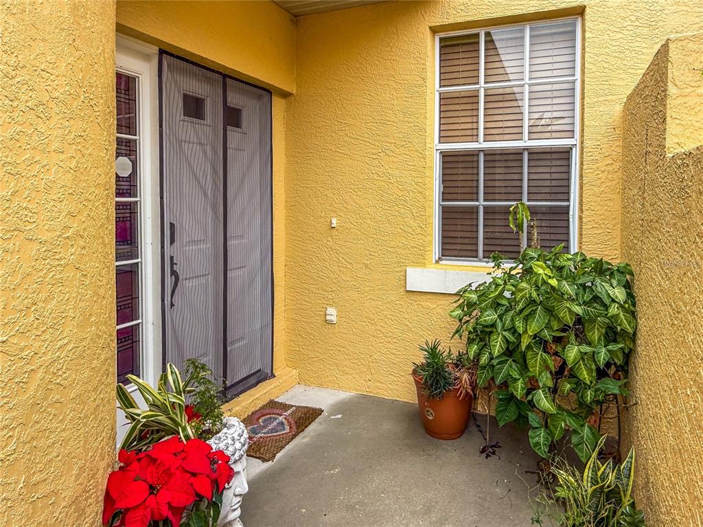 A yellow stucco entryway features a front door with a screen, a window, and potted plants — 5715 SPANISH POINT COURT, PALMETTO, FL