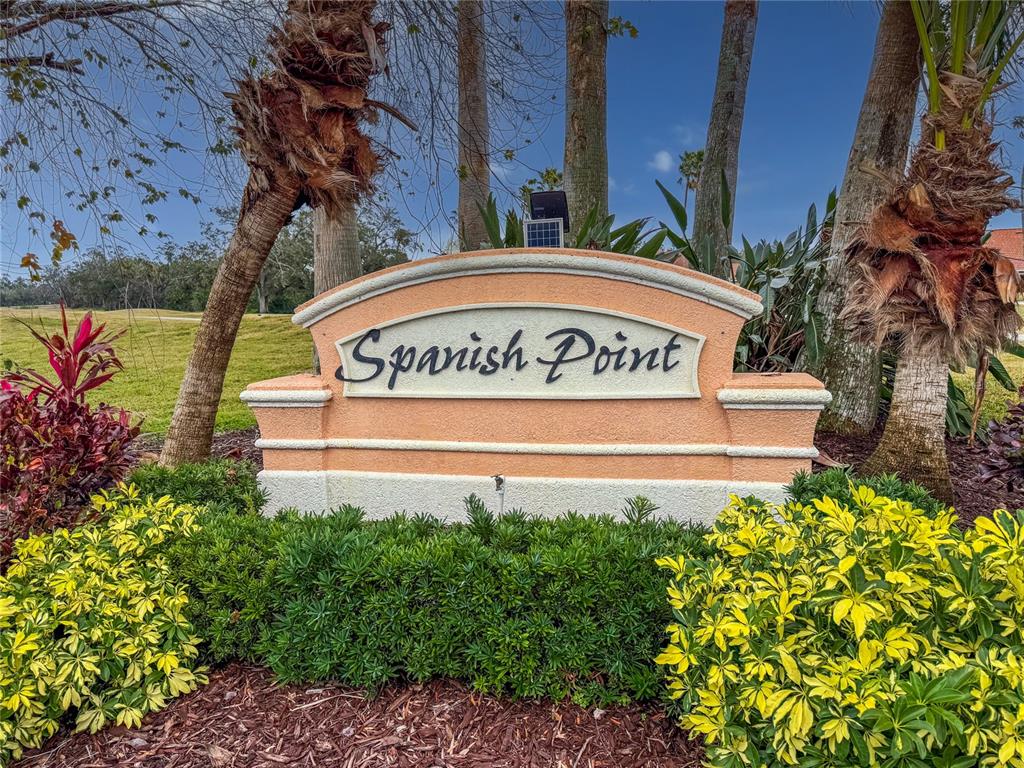 A peach-colored monument sign for Spanish Point stands in a landscaped garden with palm trees — 5715 SPANISH POINT COURT, PALMETTO, FL