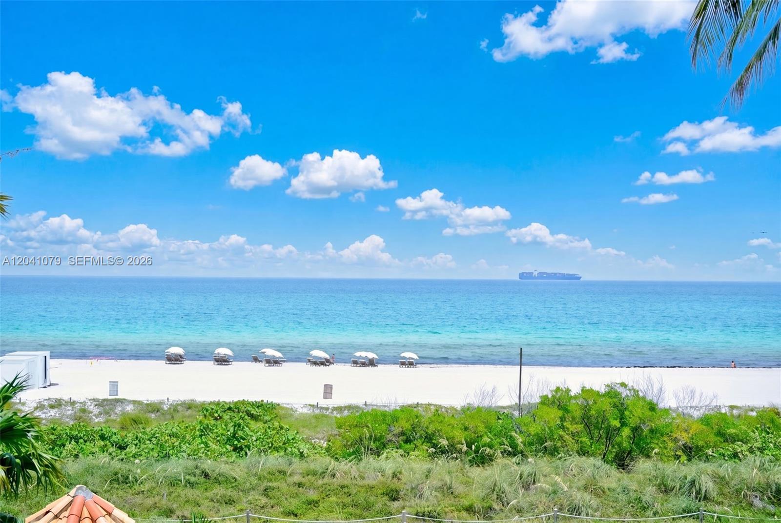 A view of a white sand beach with umbrellas and a cargo ship offshore — 5757 Collins Ave # 405, Miami Beach FL 33140, MIAMI BEACH, FL