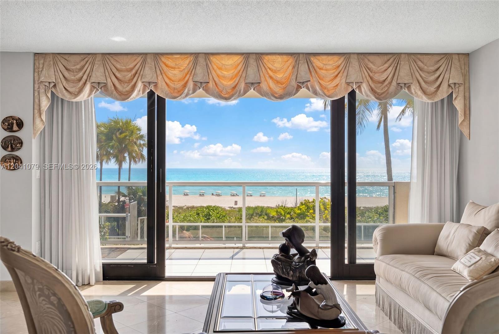 A living room with a beige sofa overlooks a balcony and the ocean beyond — 5757 Collins Ave # 405, Miami Beach FL 33140, MIAMI BEACH, FL
