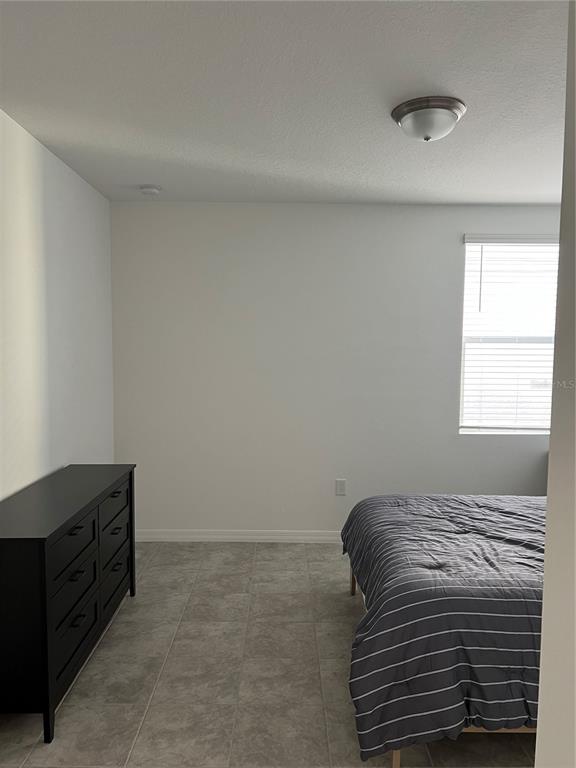 A bedroom with tiled floors, a black dresser, a bed with striped bedding, and a window — 4932 MAINSAIL STREET, HAINES CITY, FL