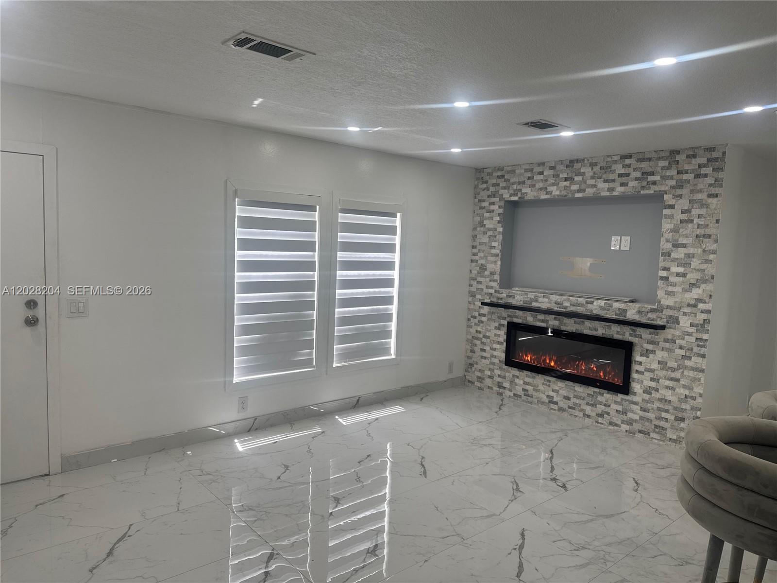A living room features white marble-look tile floors, a stone-tiled fireplace wall, and two windows — 720 N Riverside St, Clewiston FL 33440, CLEWISTON, FL