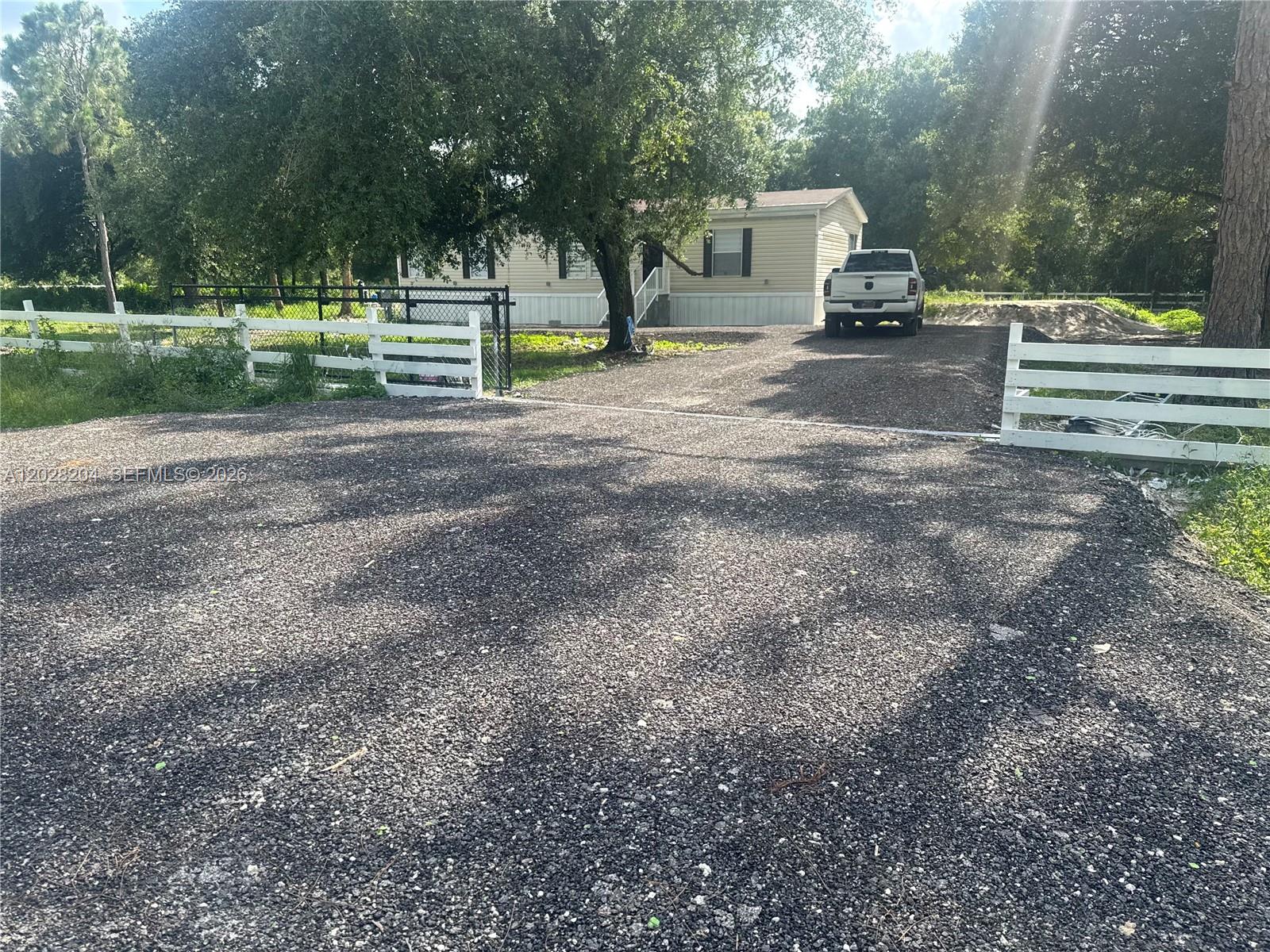 A gravel driveway leads to a single-story house behind a white wooden fence — 720 N Riverside St, Clewiston FL 33440, CLEWISTON, FL
