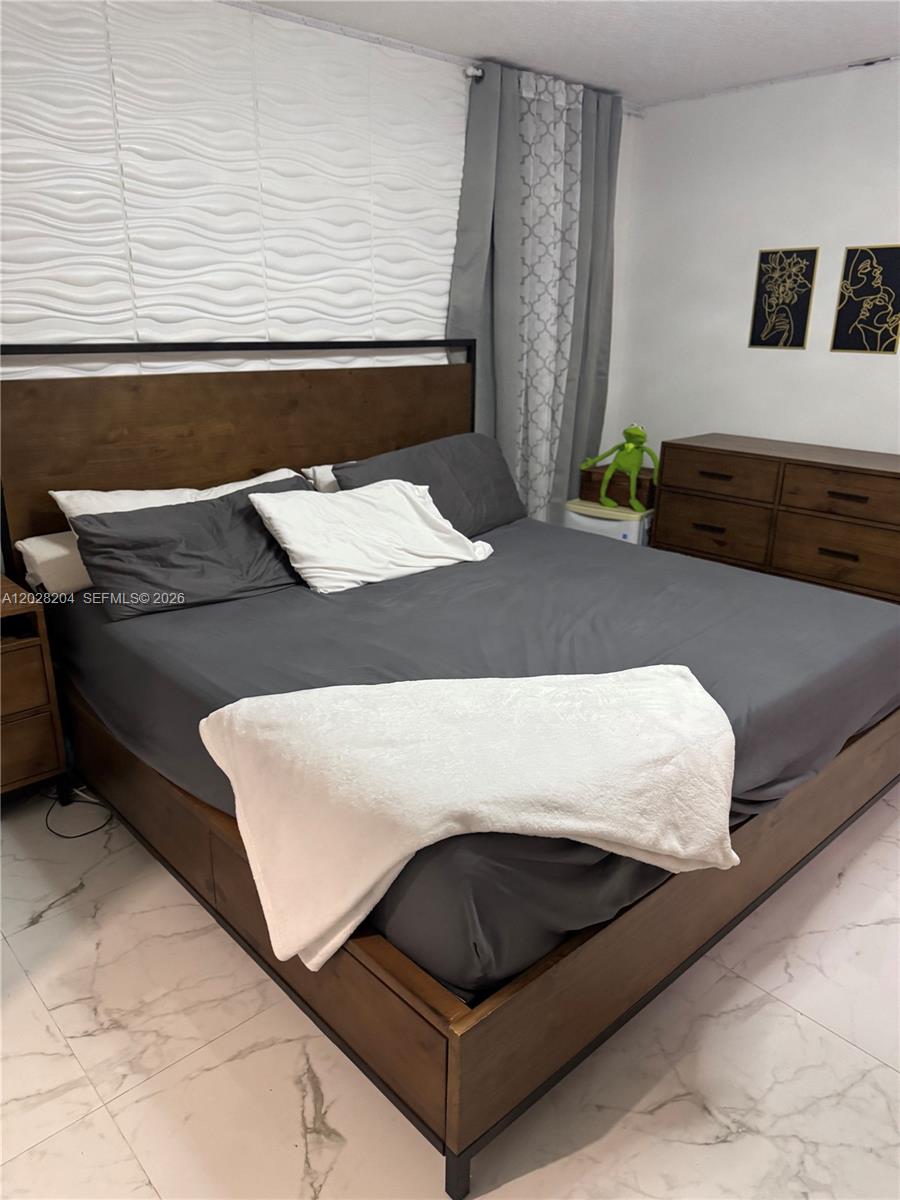 A bedroom features a wooden bed frame, gray bedding, and a textured white accent wall — 720 N Riverside St, Clewiston FL 33440, CLEWISTON, FL