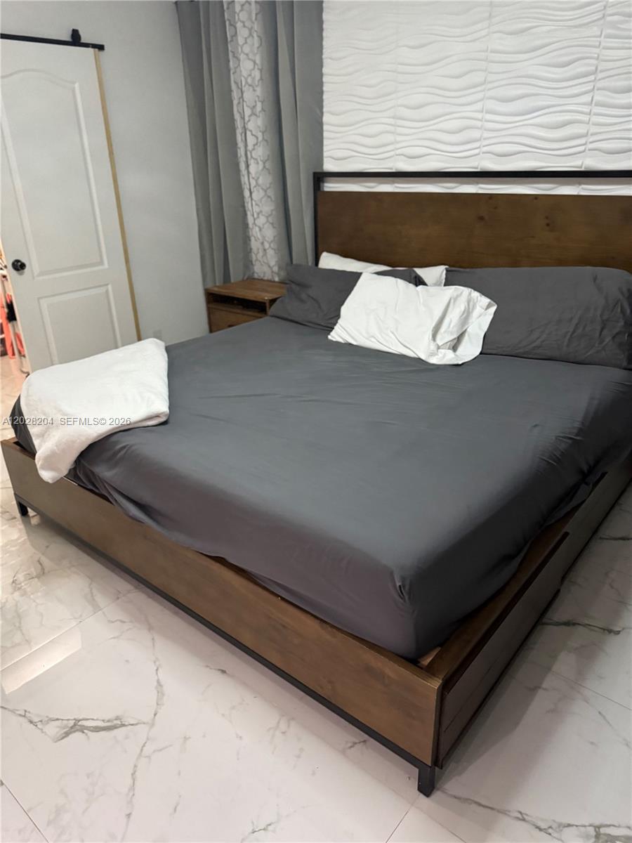 A bedroom features a wooden bed frame, gray bedding, and a textured white accent wall — 720 N Riverside St, Clewiston FL 33440, CLEWISTON, FL