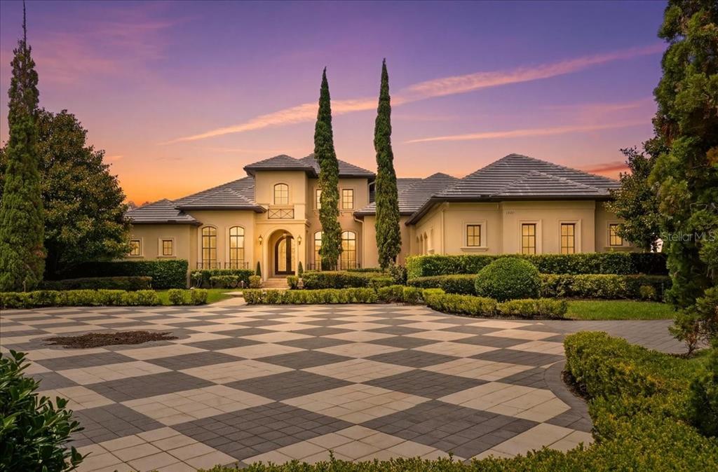 A large two-story house with a checkered stone driveway and tall cypress trees at dusk — 13431 BELLARIA CIRCLE, WINDERMERE, FL