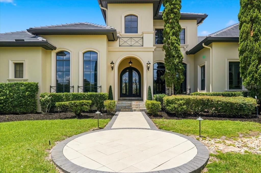 A two-story stucco house with a tiled roof, arched entryway, and a paved circular walkway — 13431 BELLARIA CIRCLE, WINDERMERE, FL